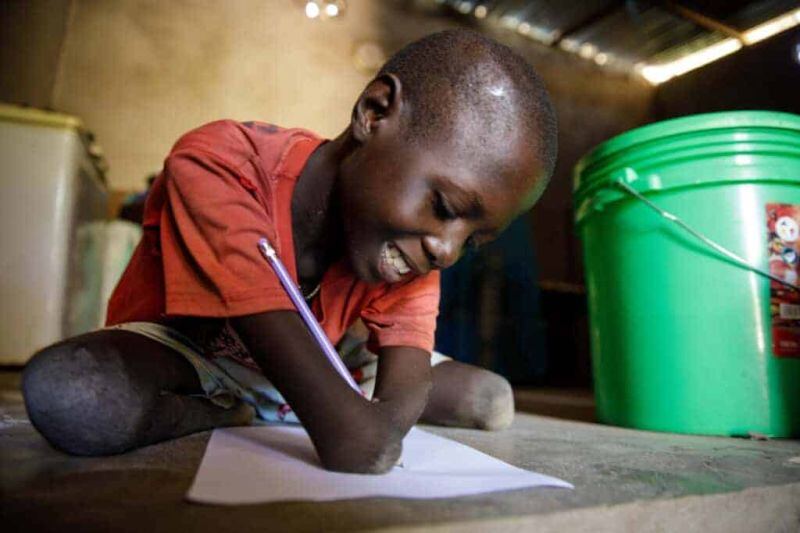 Child with disability writing and smiling